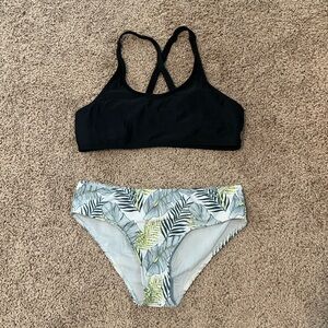 This is a kids bikini with a black top and shades of green tropical bottoms.